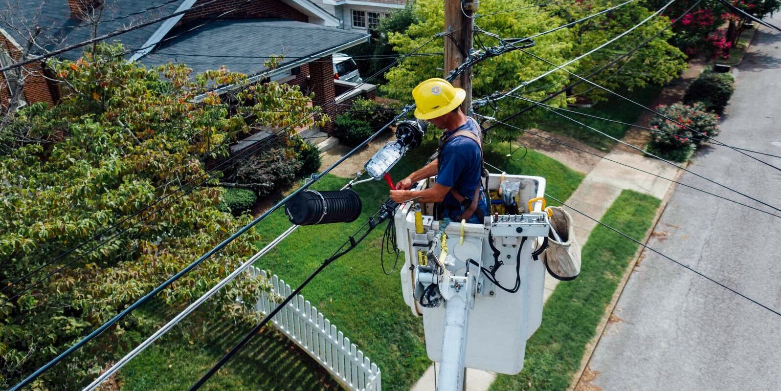 Electrician in a bucket lift repairing power lines from a utility pole in a suburban neighborhood.