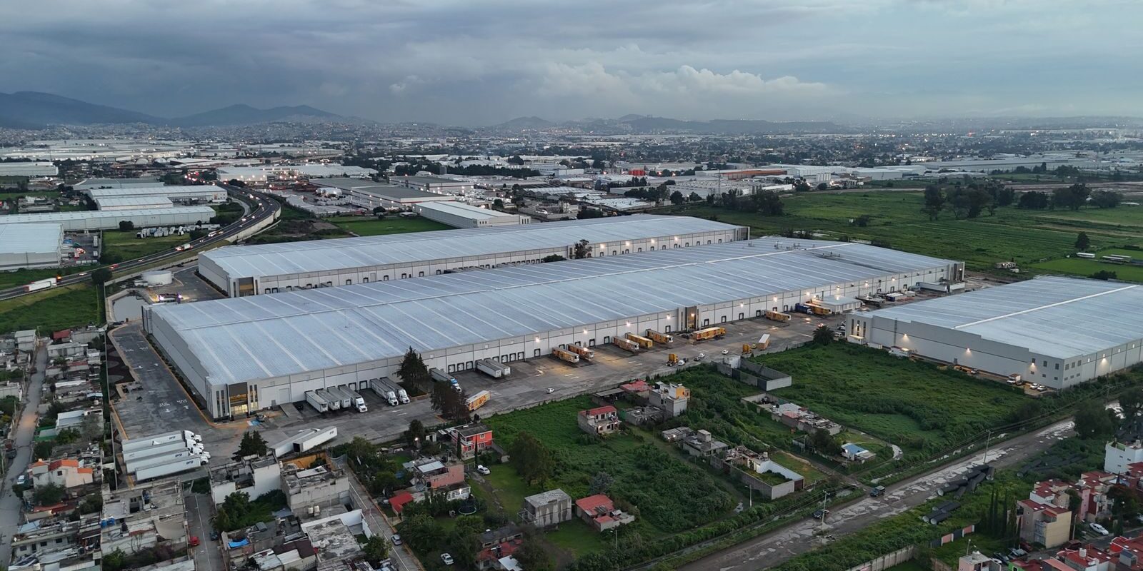 Aerial view of industrial warehouses in Mexico City surrounded by residential areas and greenery.