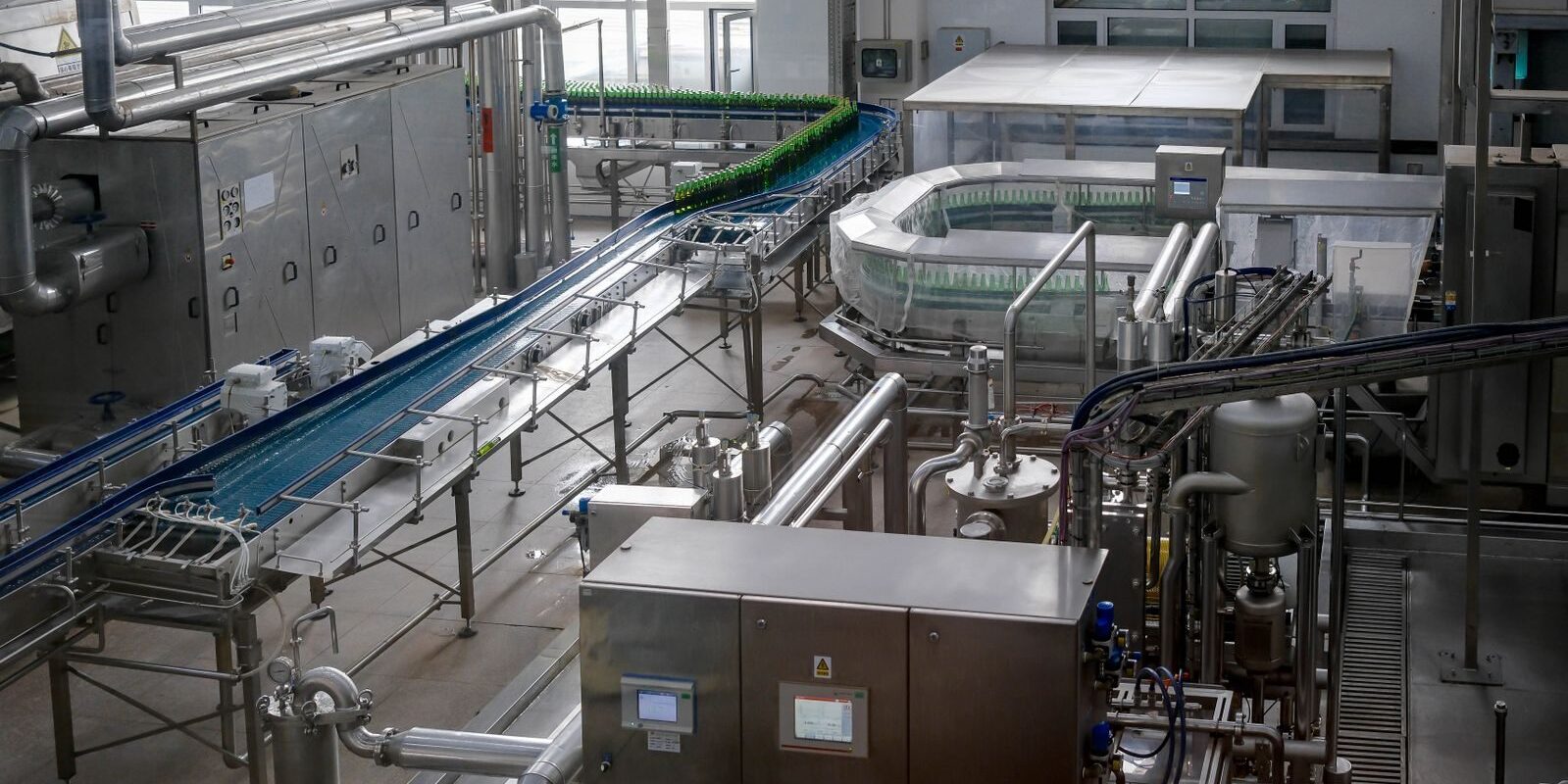 Photo by BI ravencrow Interior view of an automated beverage bottling factory with machinery and conveyor belts.