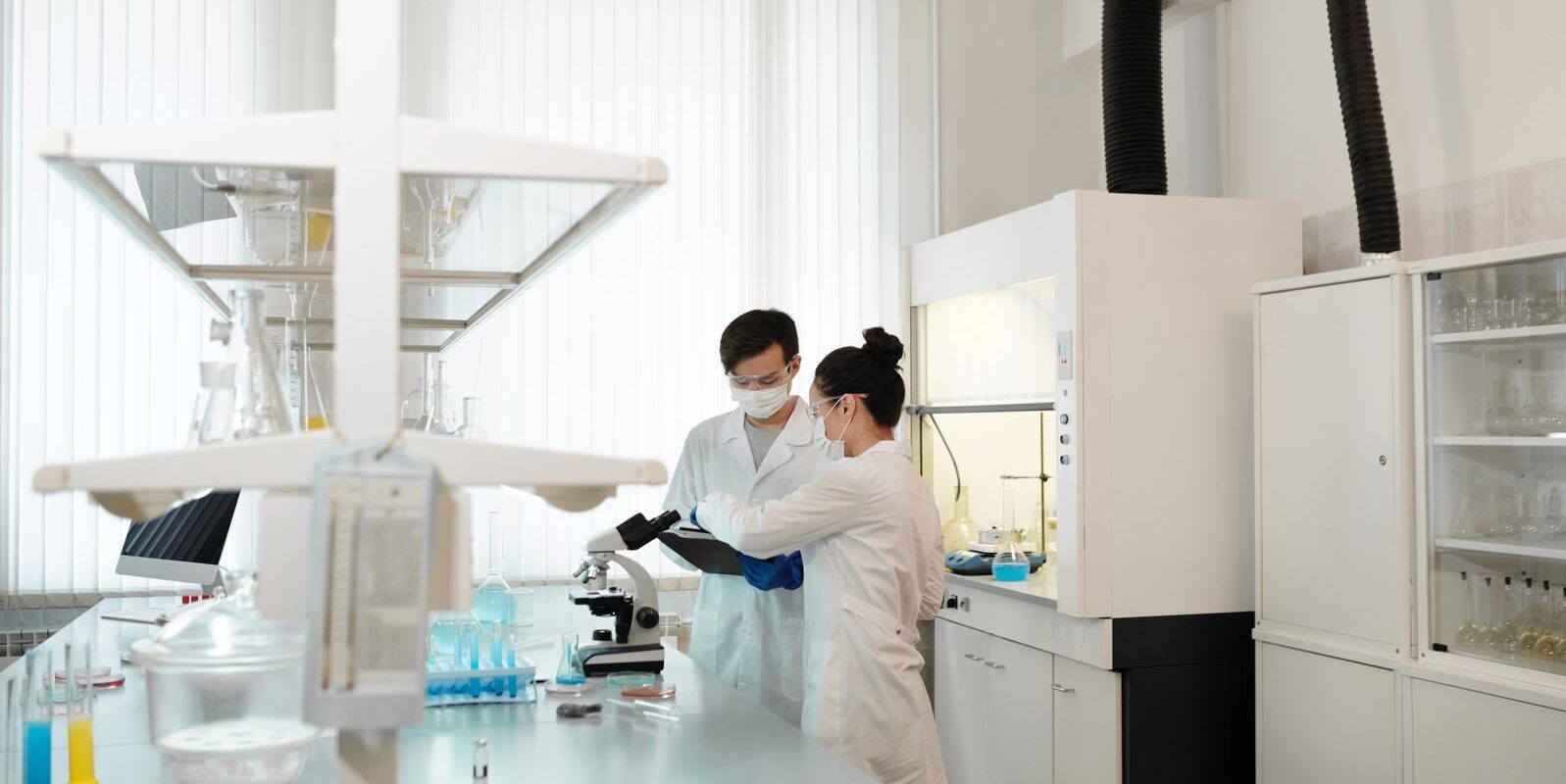 Two scientists wearing protective gear collaborating in a laboratory setting with modern equipment.