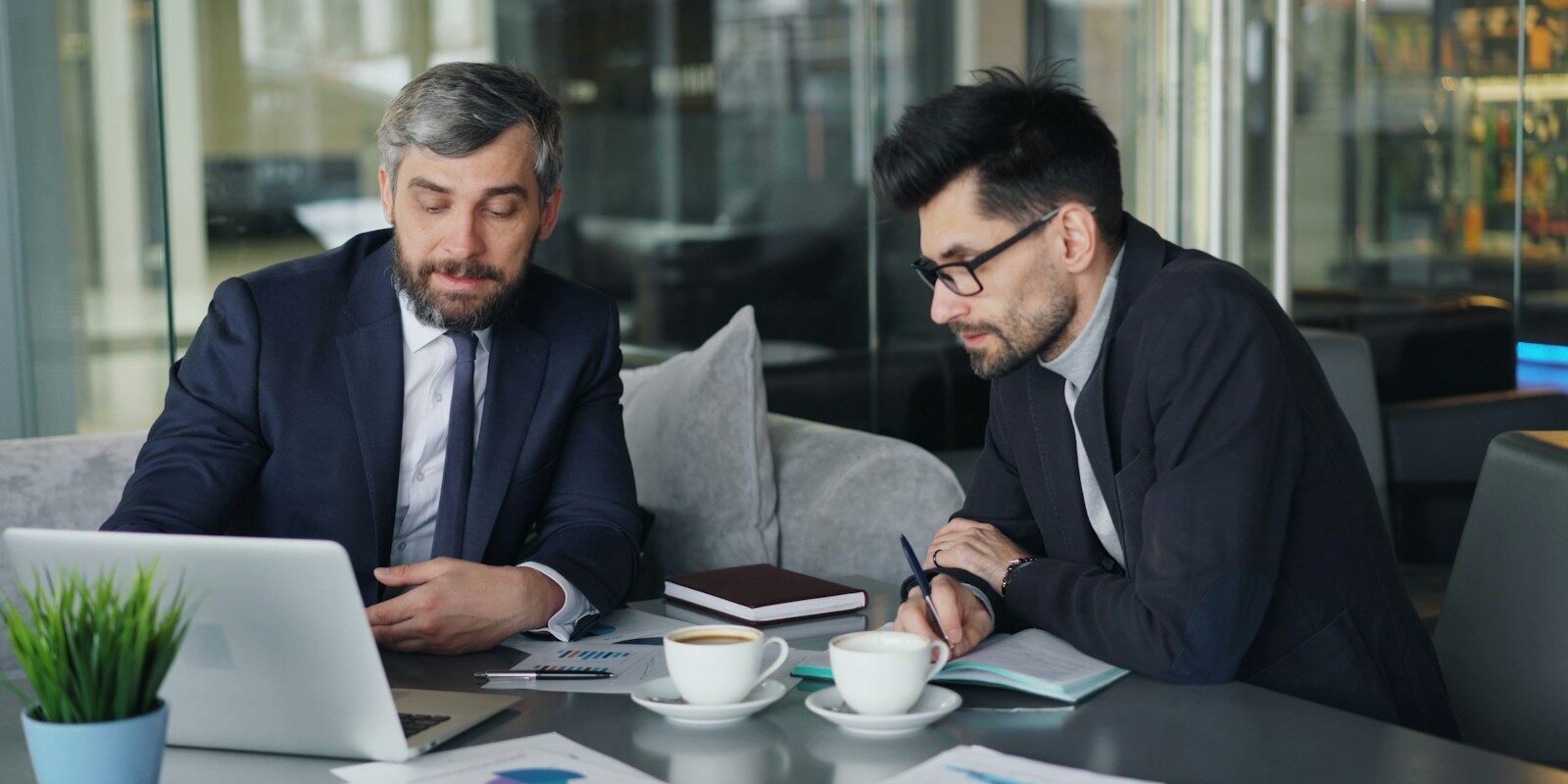 two men sitting at a table working on a laptop