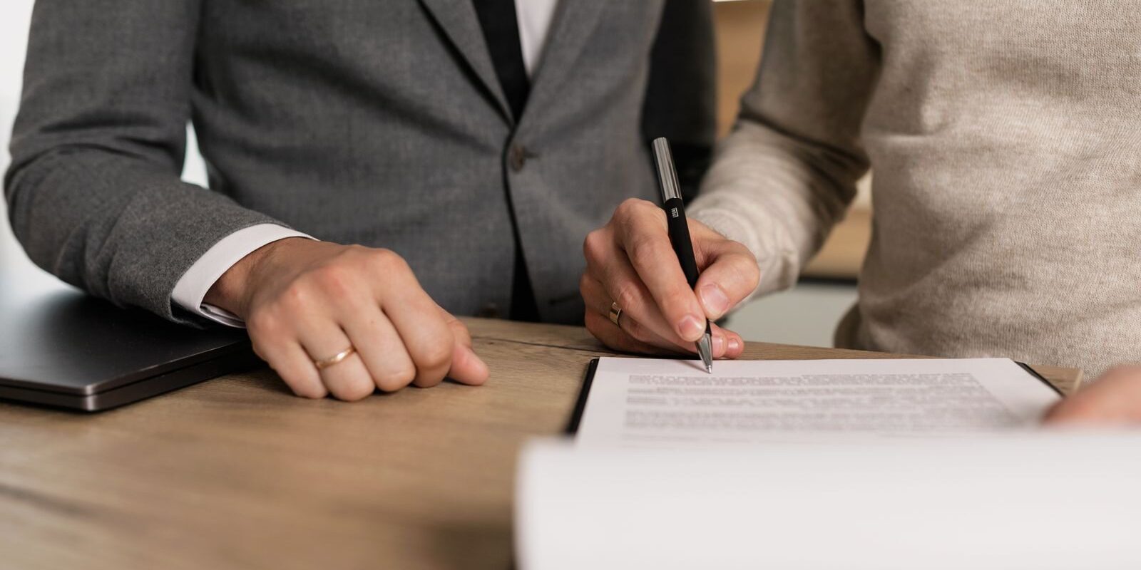 Photo by Alena Darmel Close-up of businessmen signing documents at a wooden table in an office.