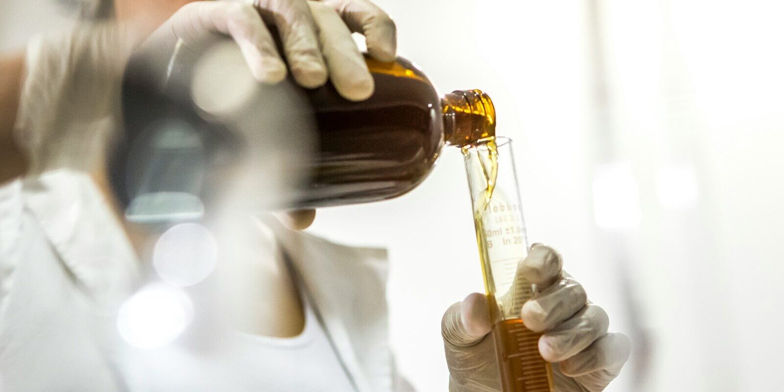 woman wearing white lab coat holding brown bottle and glass tube