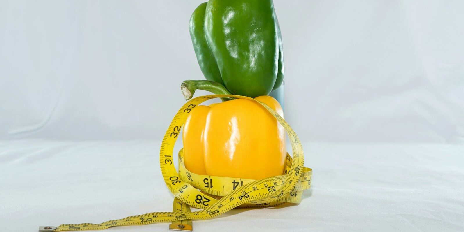 a yellow pepper and a green pepper on a measuring tape