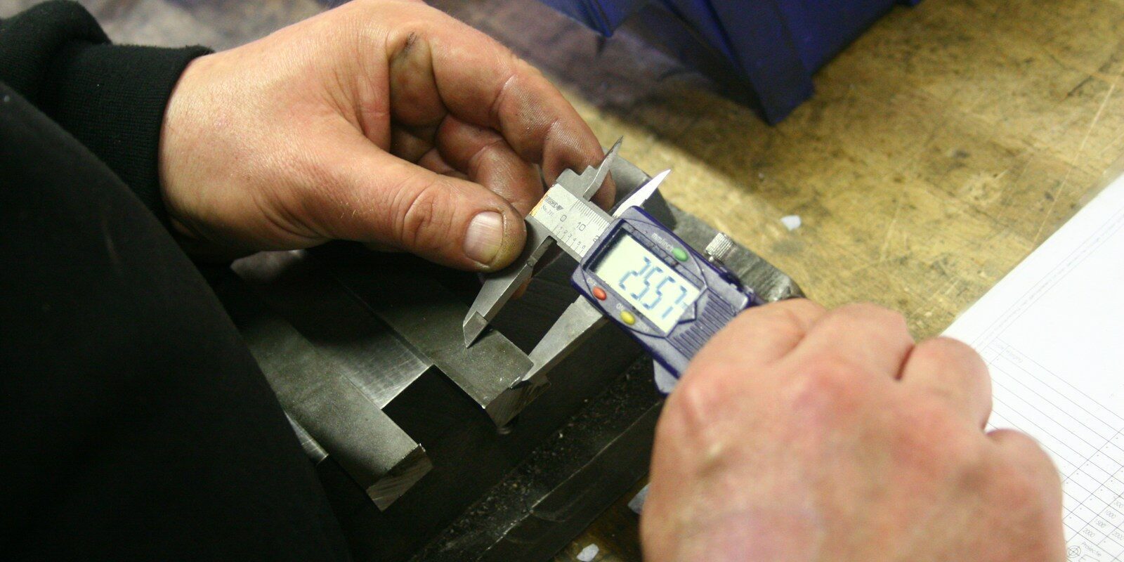 Hands using a digital caliper to measure metal part