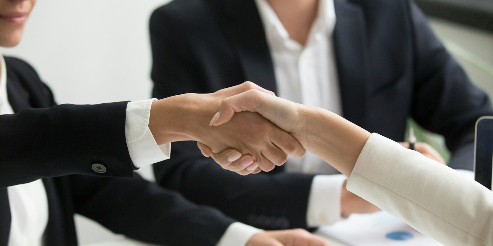 two people shaking hands in front of a laptop