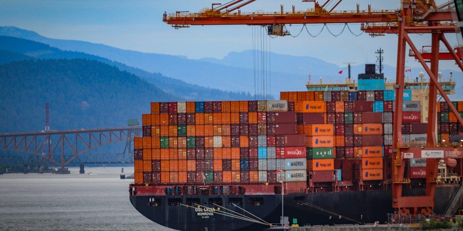 Docked cargo ship with colorful containers, cranes, and mountains